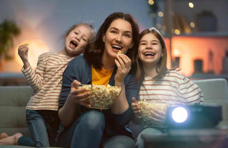 Mother and two children laughing with popcorn during a family movie night — ViviMate kids